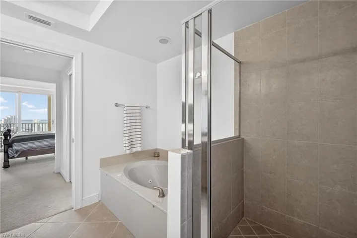 Bathroom featuring a stall shower, a tub with jets, light colored carpet, light tile patterned floors, and ensuite bathroom