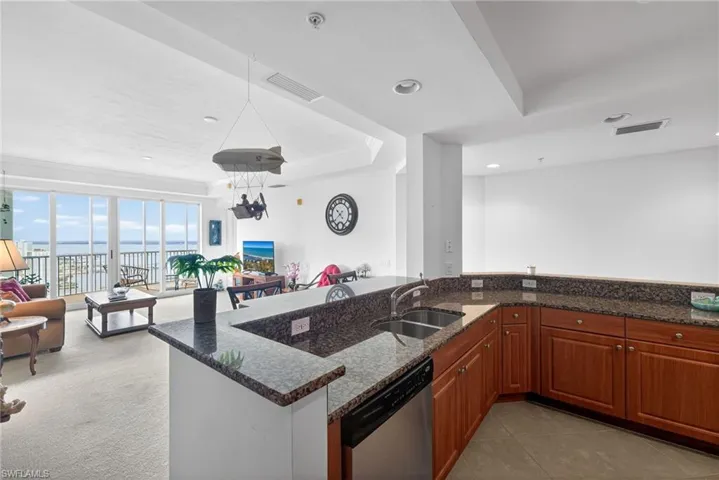 Kitchen featuring a tray ceiling, dark stone counters, open floor plan, stainless steel dishwasher, and wood finish cabinets