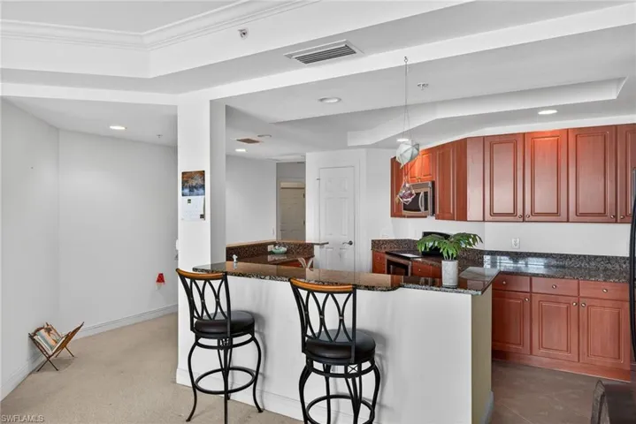Kitchen with a kitchen breakfast bar, dark stone countertops, recessed lighting, stainless steel appliances, and wood finish cabinets