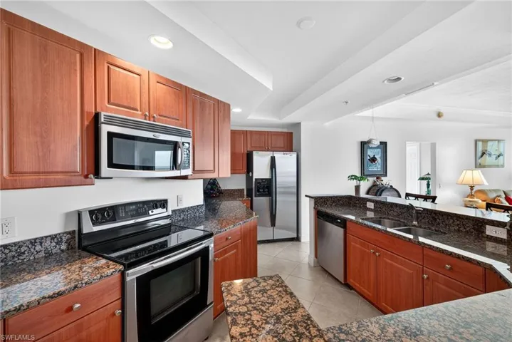 Kitchen featuring stainless steel appliances, dark stone counters, wood finish cabinetry, open floor plan, and hanging light fixtures