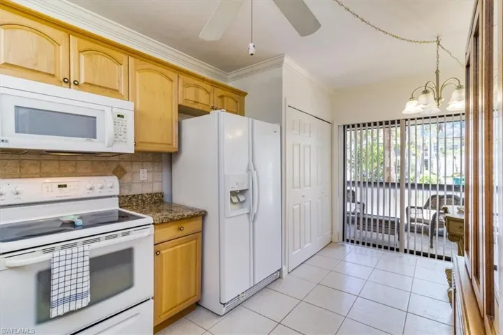 Kitchen with tasteful backsplash, white appliances, pendant lighting, light tile patterned floors, and ceiling fan with notable chandelier