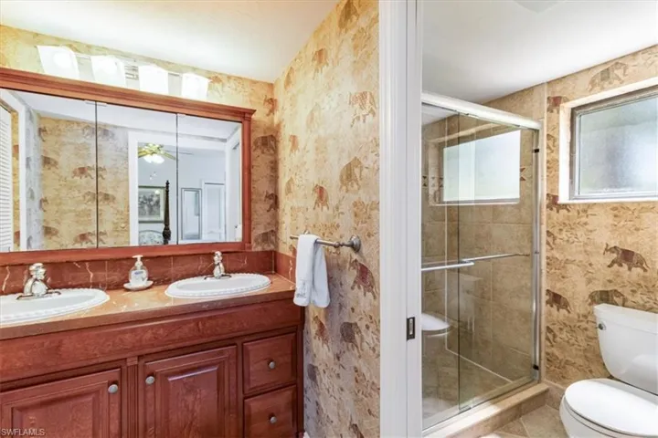 Bathroom with an enclosed shower, tile patterned flooring, toilet, and double sink vanity