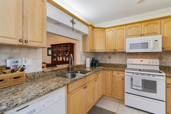 Kitchen featuring light tile patterned flooring, white appliances, sink, stone countertops, and backsplash