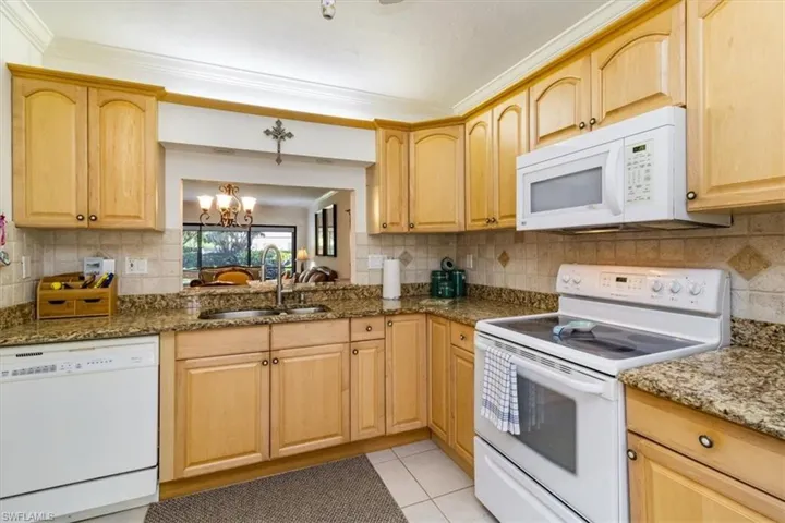 Kitchen with crown molding, white appliances, a chandelier, dark stone counters, and sink