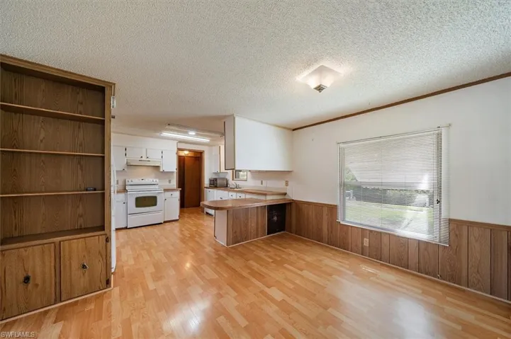 Kitchen with wainscoting, a peninsula, wood walls, electric stove, and white cabinets