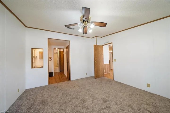 Unfurnished bedroom with light carpet, ornamental molding, a textured ceiling, ceiling fan, and ensuite bath