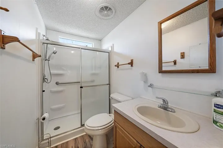 Full bathroom with vanity, a textured ceiling, a shower stall, and dark wood-style floors
