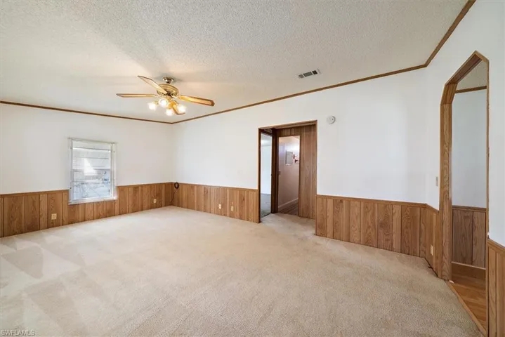 Unfurnished room with carpet flooring, ornamental molding, wooden walls, a wainscoted wall, and a textured ceiling