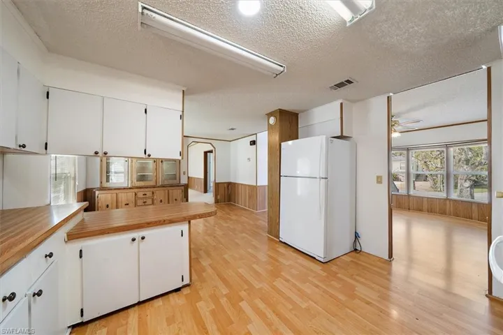 Kitchen featuring a textured ceiling, freestanding refrigerator, white cabinetry, light wood finished floors, and wood walls