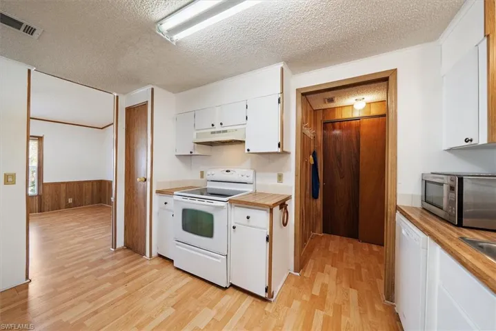 Kitchen with white cabinets, white appliances, wood walls, crown molding, and a textured ceiling
