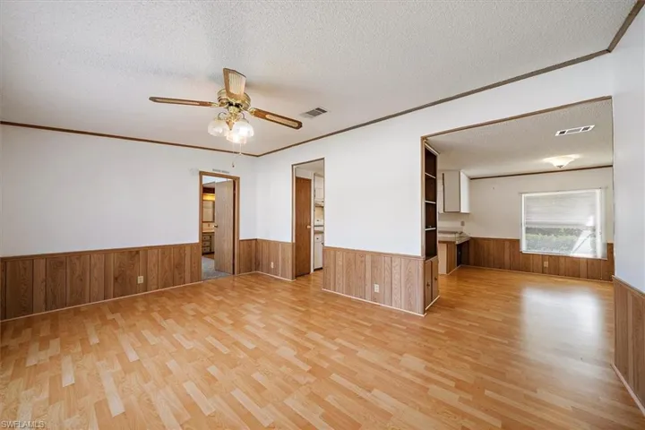 Unfurnished room with a textured ceiling, wainscoting, ceiling fan, crown molding, and light wood-style flooring