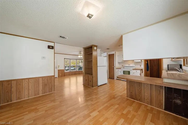 Kitchen featuring a wainscoted wall, wooden walls, white appliances, a textured ceiling, and white cabinets