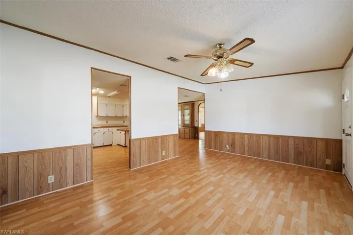 Spare room featuring a textured ceiling, a ceiling fan, crown molding, light wood-style flooring, and wainscoting