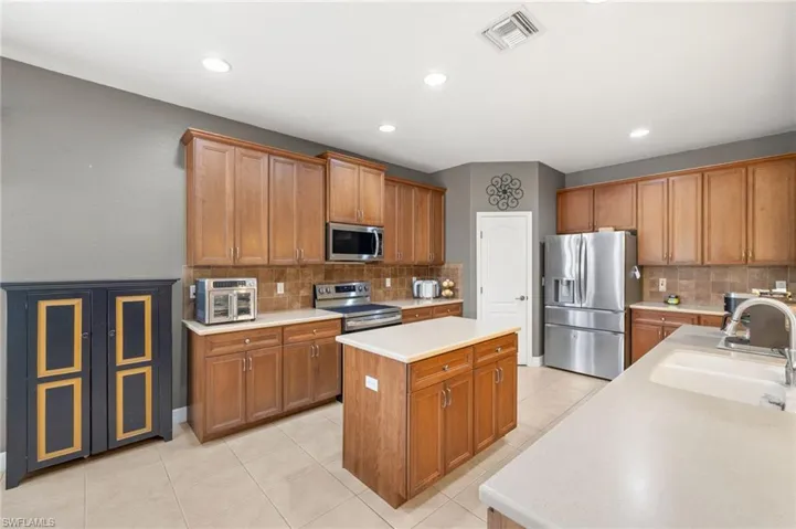 Kitchen featuring a kitchen island, backsplash, visible vents, a sink, and stainless steel appliances