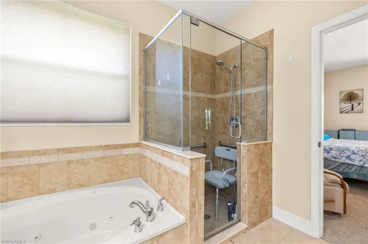 Full bathroom featuring connected bathroom, tile patterned floors, a whirlpool tub, baseboards, and a stall shower