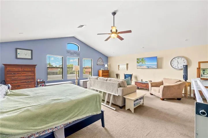 Large loft area being used as a bedroom, featuring carpet floors, a ceiling fan, vaulted ceiling, and visible vents