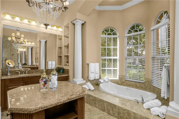 Full bath featuring decorative columns, built in features, a garden tub, hanging lights, and vanity