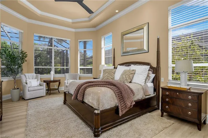 Bedroom with light wood finished floors, a ceiling fan, a tray ceiling, and ornamental molding