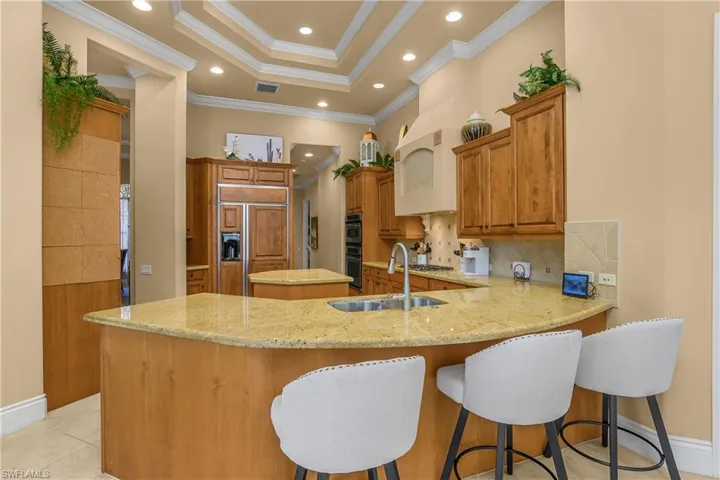 Kitchen featuring light stone counters, wood finish cabinets, paneled built in refrigerator, a tray ceiling, and a breakfast bar area