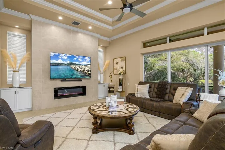 Living room featuring crown molding, ceiling fan, tile walls, a high tray ceiling, and light tile patterned floors