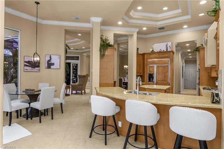 Kitchen featuring wood finish cabinets, light stone countertops, ornamental molding, a tray ceiling, and paneled built in fridge