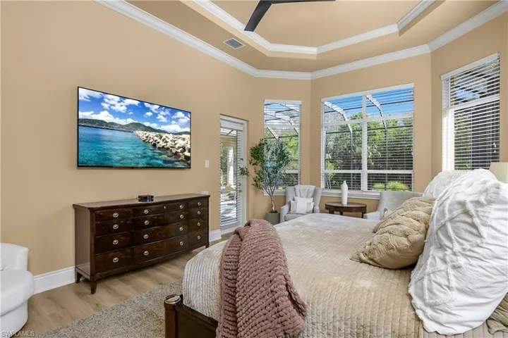 Bedroom featuring access to exterior, wood finished floors, ornamental molding, ceiling fan, and a tray ceiling