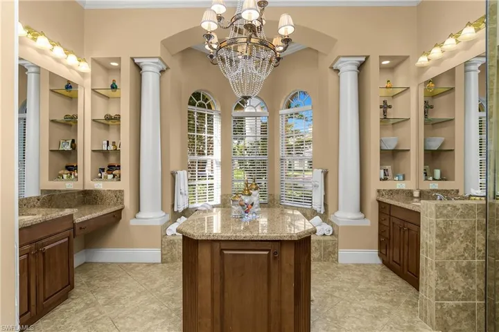 Full bathroom featuring decorative columns, crown molding, two vanities, built in features, and hanging lights