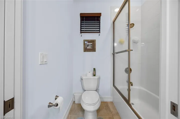 Bathroom featuring toilet, shower / bath combination with glass door, and tile patterned flooring
