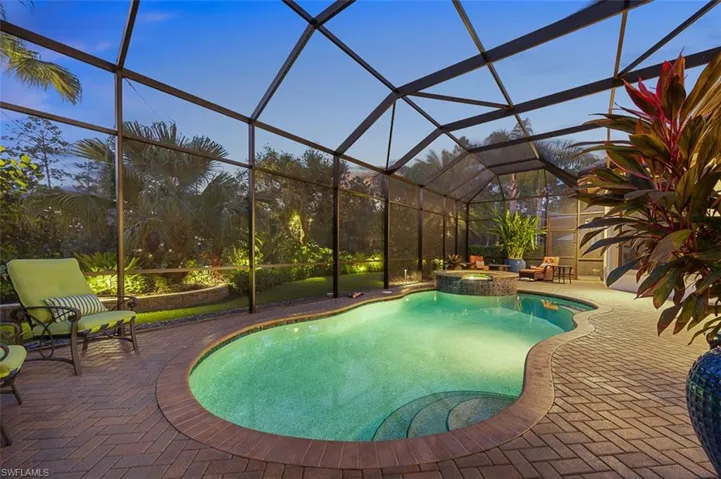 Pool at dusk with an in ground hot tub, a patio area, and a lanai