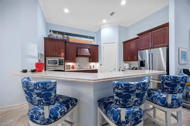 Kitchen with a kitchen breakfast bar, custom range hood, tasteful backsplash, crown molding, and stainless steel appliances