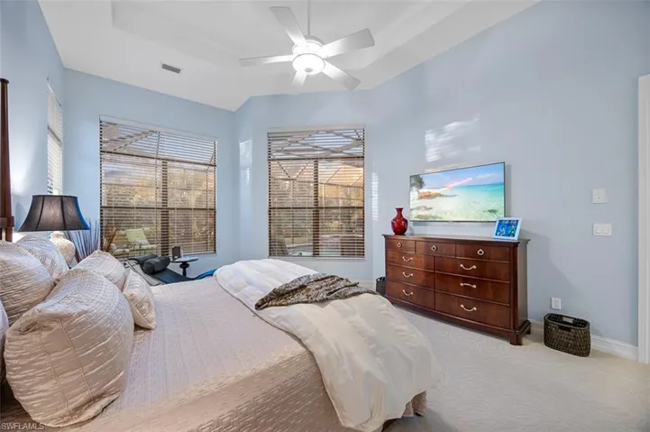 Carpeted bedroom featuring a raised ceiling, ceiling fan, and ornamental molding