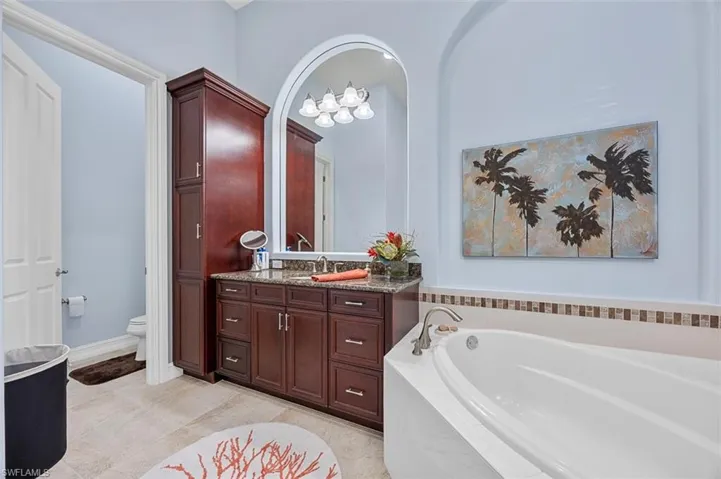 Bathroom featuring vanity, a relaxing tiled tub, toilet, and tile patterned floors