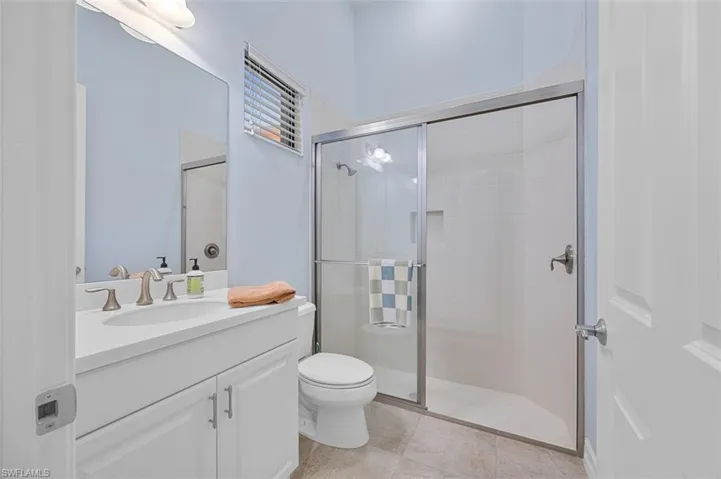 Bathroom featuring tile patterned floors, vanity, toilet, and a shower with door