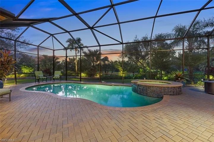 Pool at dusk featuring a lanai, an in ground hot tub, and a patio