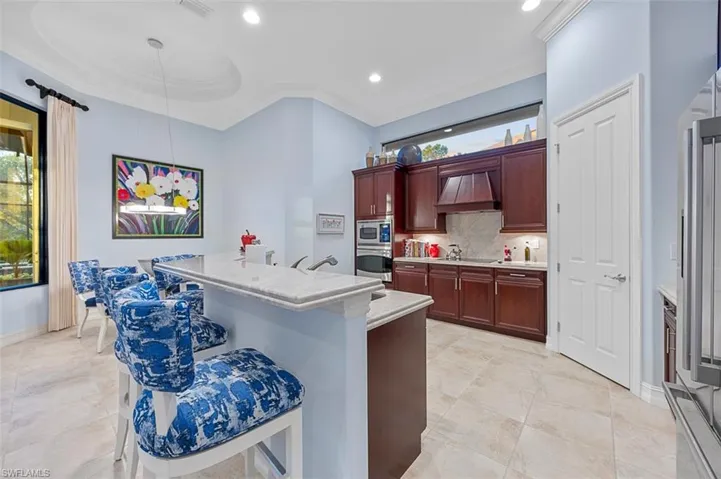 Kitchen featuring stainless steel microwave, tasteful backsplash, premium range hood, pendant lighting, and black stovetop