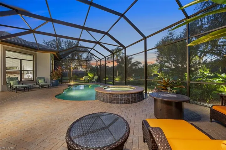 Pool at dusk featuring glass enclosure, a patio area, and an in ground hot tub
