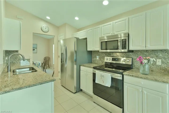 Kitchen featuring light stone countertops, stainless steel appliances, white cabinetry, vaulted ceiling, and light tile patterned floors