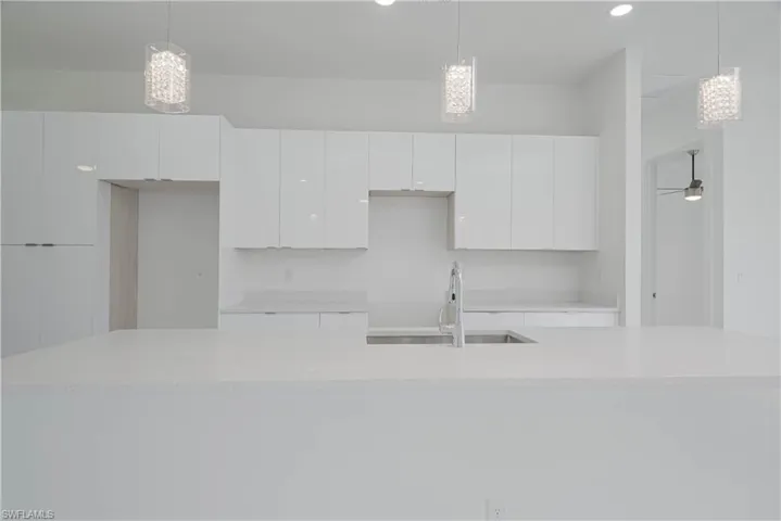 Kitchen featuring white cabinetry, light countertops, a sink, and decorative light fixtures