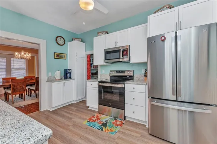 Kitchen featuring stainless steel appliances, a chandelier, light wood-type flooring, white cabinetry, and ceiling fan
