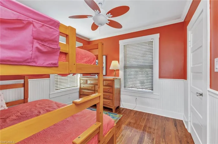 Bedroom with wood-type flooring, a wainscoted wall, ornamental molding, and ceiling fan
