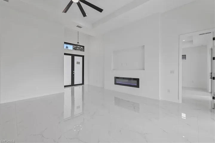 Unfurnished living room with a glass covered fireplace, a towering ceiling, a ceiling fan, and a tray ceiling