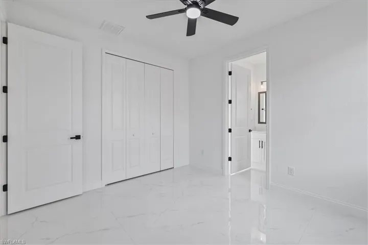 Unfurnished bedroom with ceiling fan, a closet, light marble finish floors, and ensuite bathroom