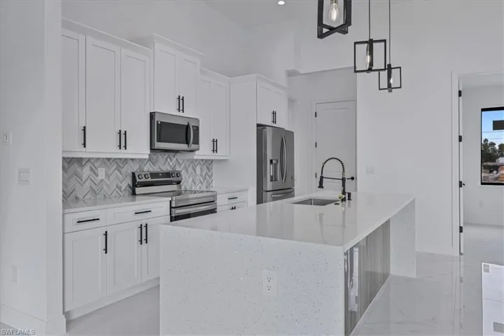 Kitchen with appliances with stainless steel finishes, white cabinets, hanging light fixtures, light stone countertops, and tasteful backsplash