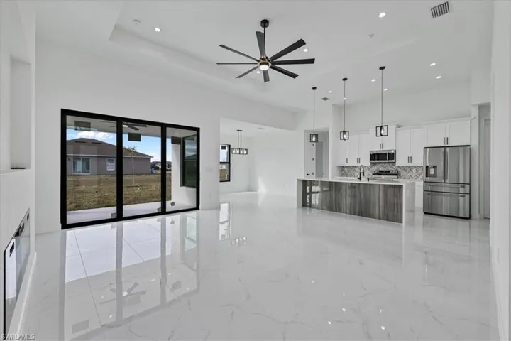 Kitchen with open floor plan, white cabinets, appliances with stainless steel finishes, a large island with sink, and decorative backsplash