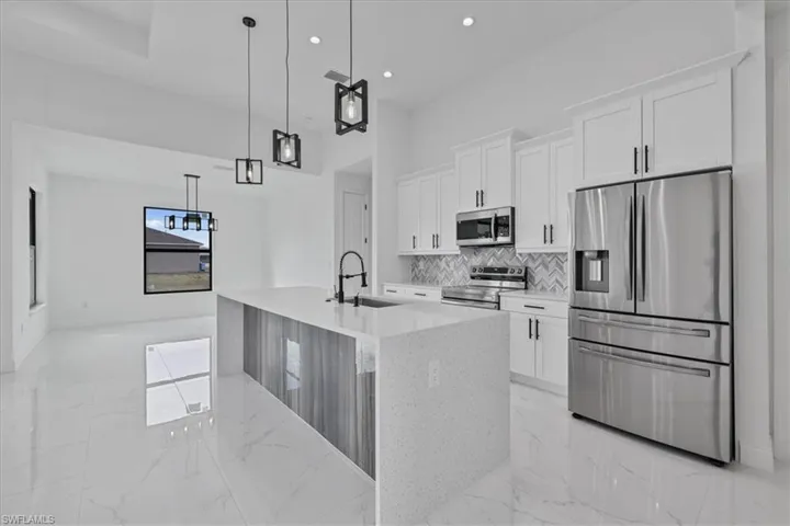 Kitchen featuring light marble finish floors, stainless steel appliances, a kitchen island with sink, white cabinets, and recessed lighting
