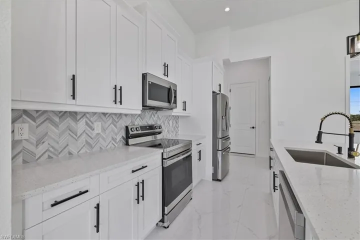 Kitchen with appliances with stainless steel finishes, light stone counters, white cabinetry, light marble finish floors, and backsplash