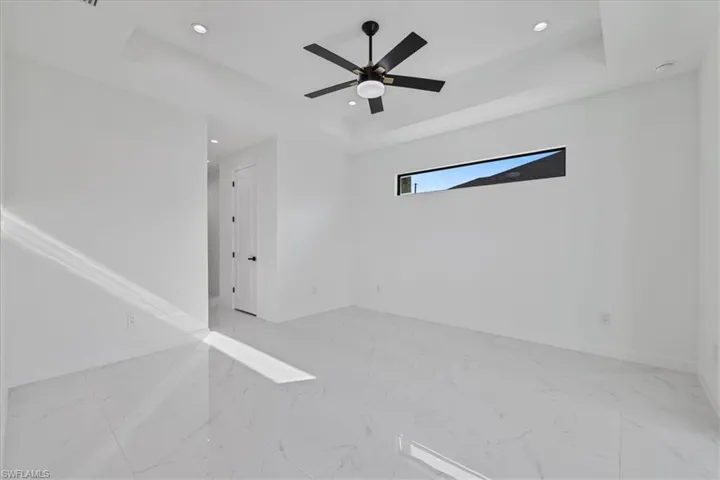 Spare room featuring light marble finish floors, a tray ceiling, recessed lighting, and a ceiling fan