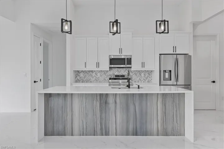Kitchen featuring light stone countertops, light marble finish flooring, stainless steel appliances, and a kitchen island with sink
