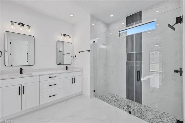 Bathroom with a marble finish shower, double vanity, recessed lighting, and light marble finish floors