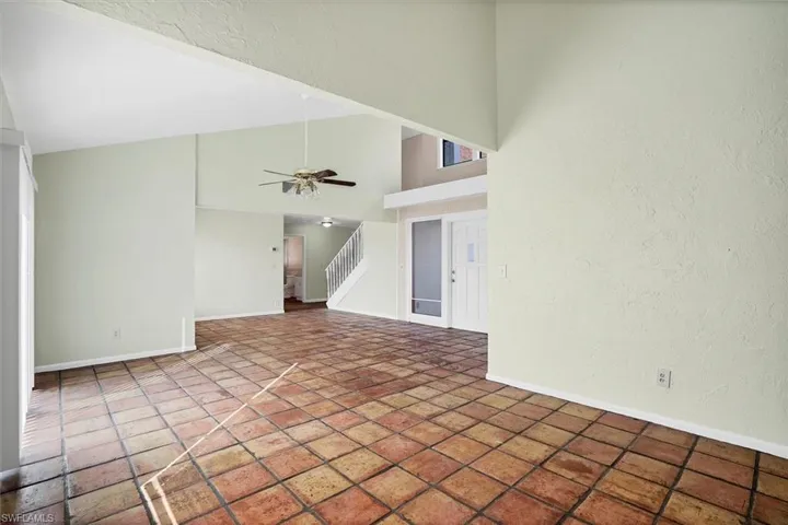 Unfurnished living room featuring stairway, high vaulted ceiling, a textured wall, and a ceiling fan